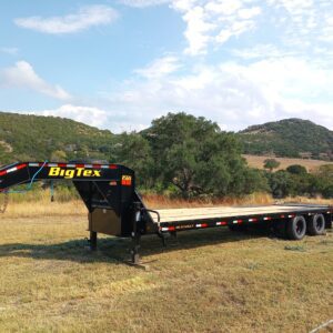 A large flatbed trailer parked in a grassy field under a partly cloudy sky.