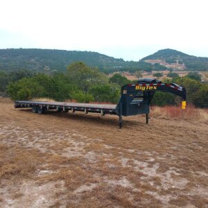 Flatbed trailer parked on a muddy ground with hills in the background.
