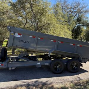 A gray dump trailer with raised bed parked on a gravel path under trees.