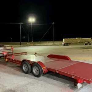 Red flatbed trailer parked at night under a bright light.