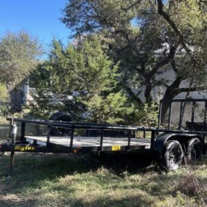 Flatbed trailer parked on grassy area under trees.